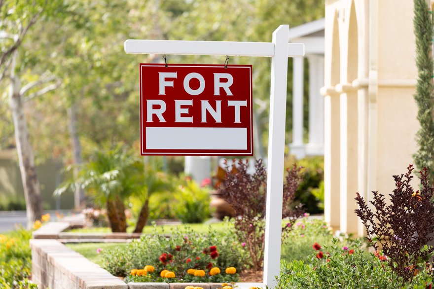 A For Rent sign in a flowerbed in front of home.