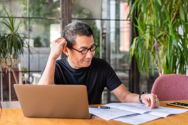 Person with laptop is looking at documents and thinking.