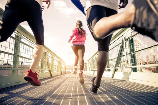 Three people in sportswear and shoes running across a bridge.
